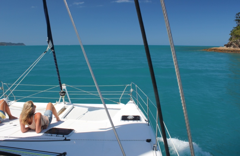 Sunbathing front deck catamaran sailing Whitsunday Islands Christmas