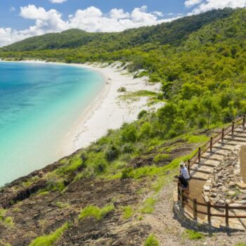 Two people standing at a fenced area, which is looking out over a beach in the Whitsunday Islands.