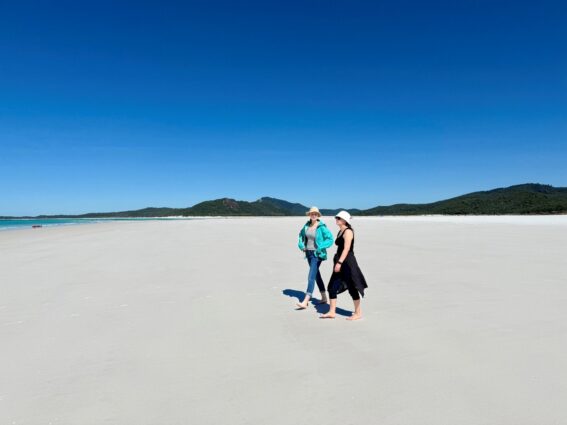 Two women walking along Whitehaven beach side by side in the sun